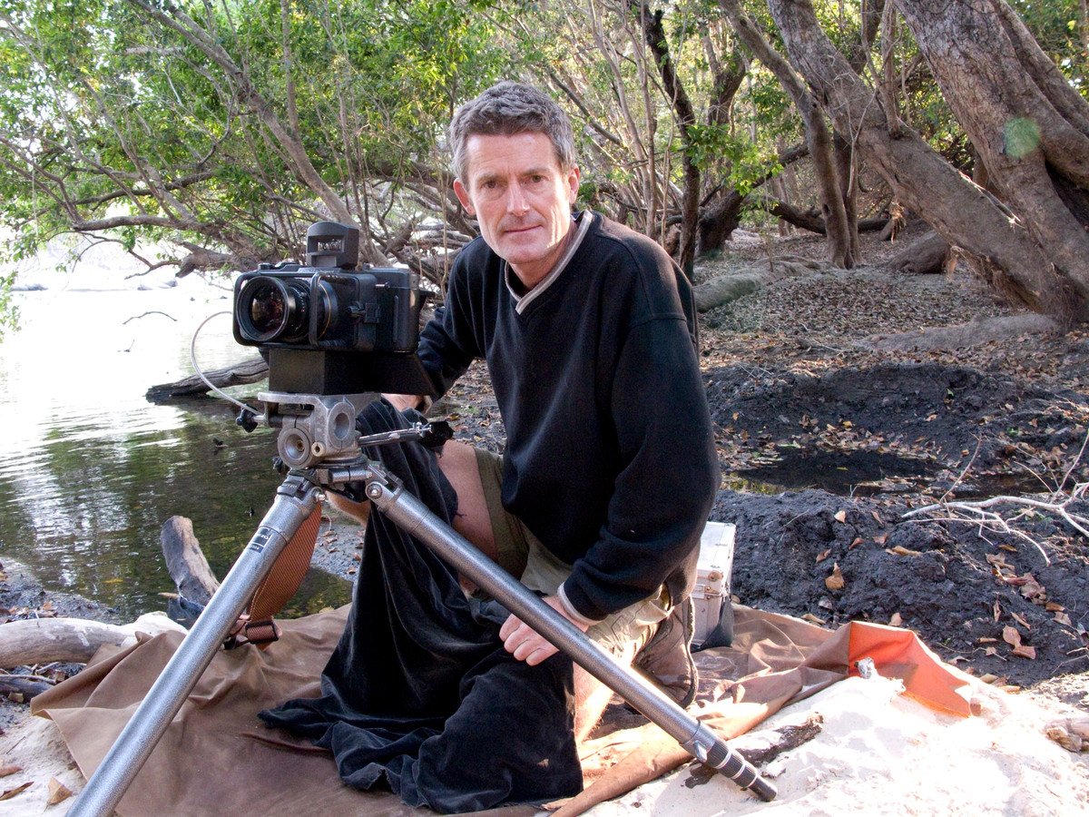 Koos van der Lende kneeling beside his panoramic camera on the bank of a river