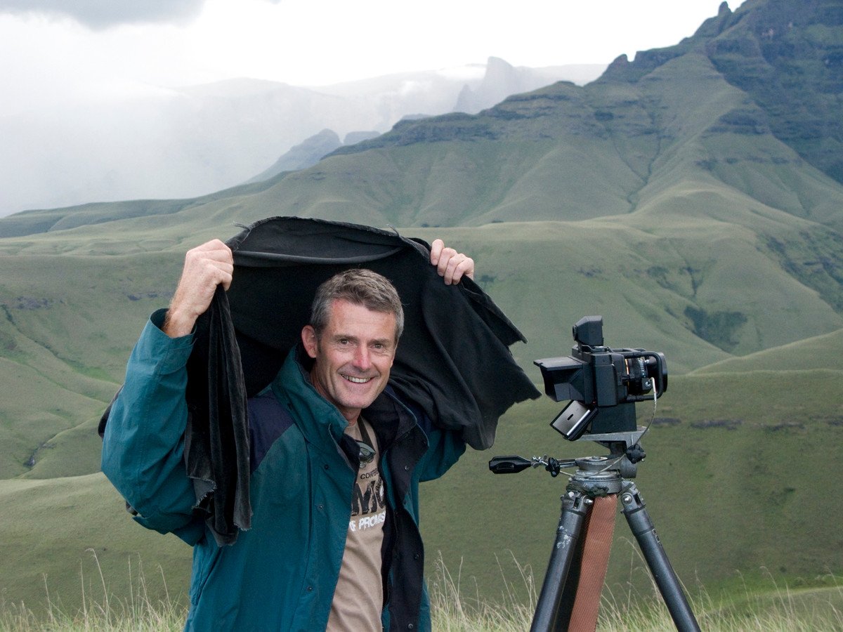 Koos van der Lende smiling under his dark cloth beside the panoramic camera, Drakensberg